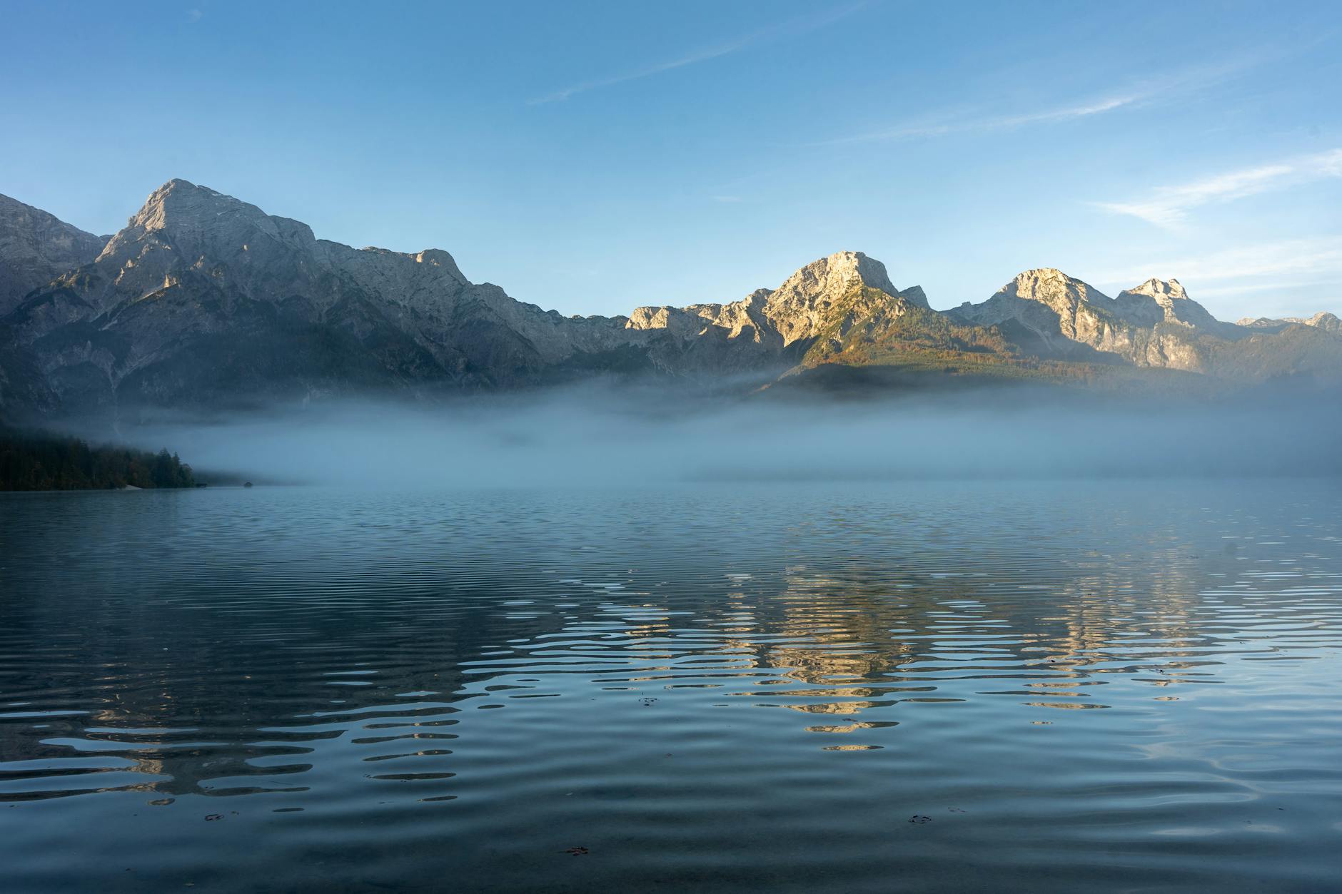 Morgendlicher Nebel über dem Alpensee mit Bergpanorama